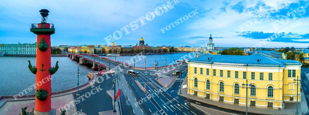 На фотографии изображена Ростральная колонна на Стрелке Васильевского острова, символизирующая морскую славу России. На заднем плане виден Дворцовый мост, соединяющий берега Невы, и величественный Исаакиевский собор. Утреннее освещение подчеркивает яркие архитектурные детали. Эта панорама демонстрирует гармонию воды, мостов и исторических зданий Санкт-Петербурга.